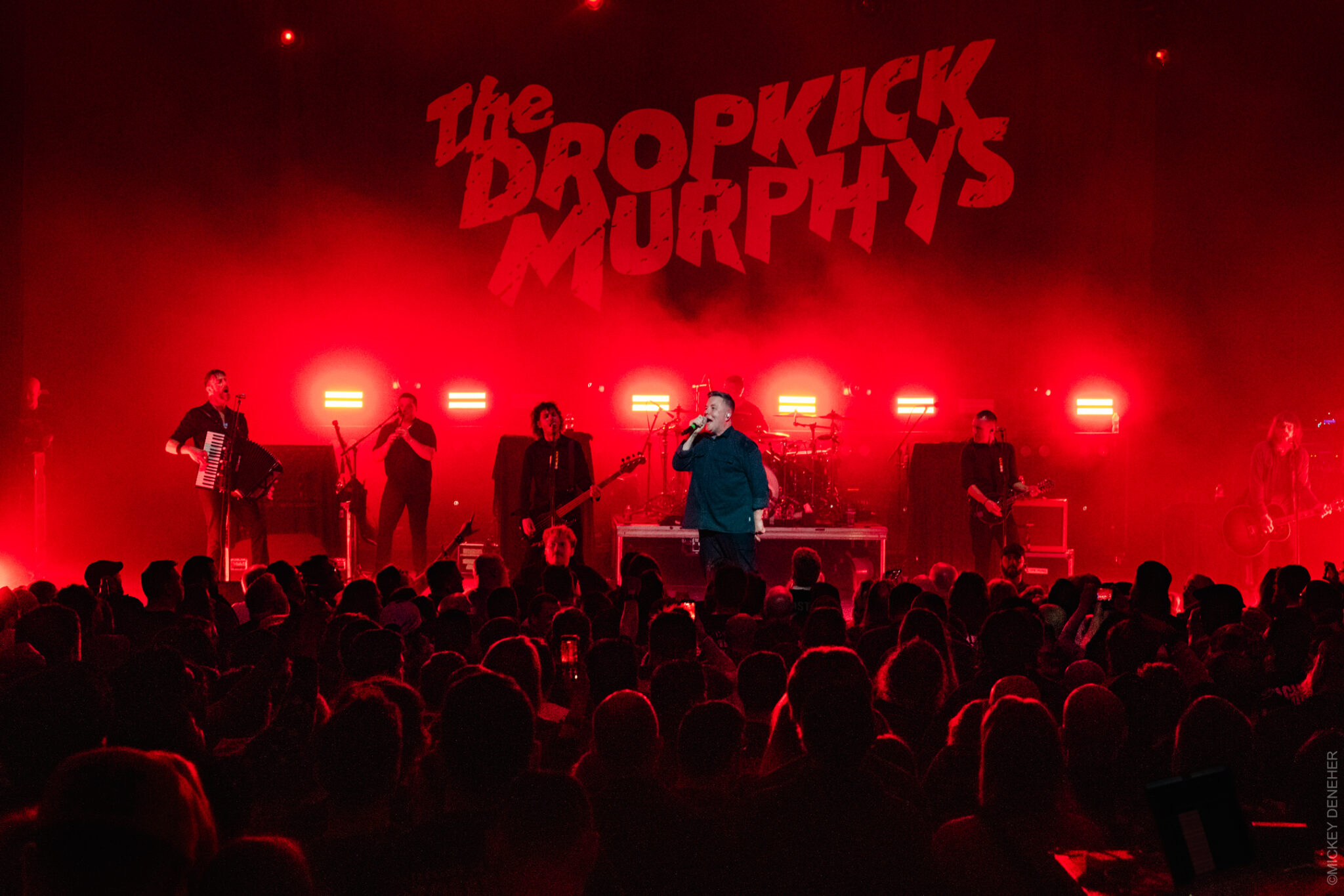Dropkick Murphys performing at a red-lit concert with the lead singer at center stage